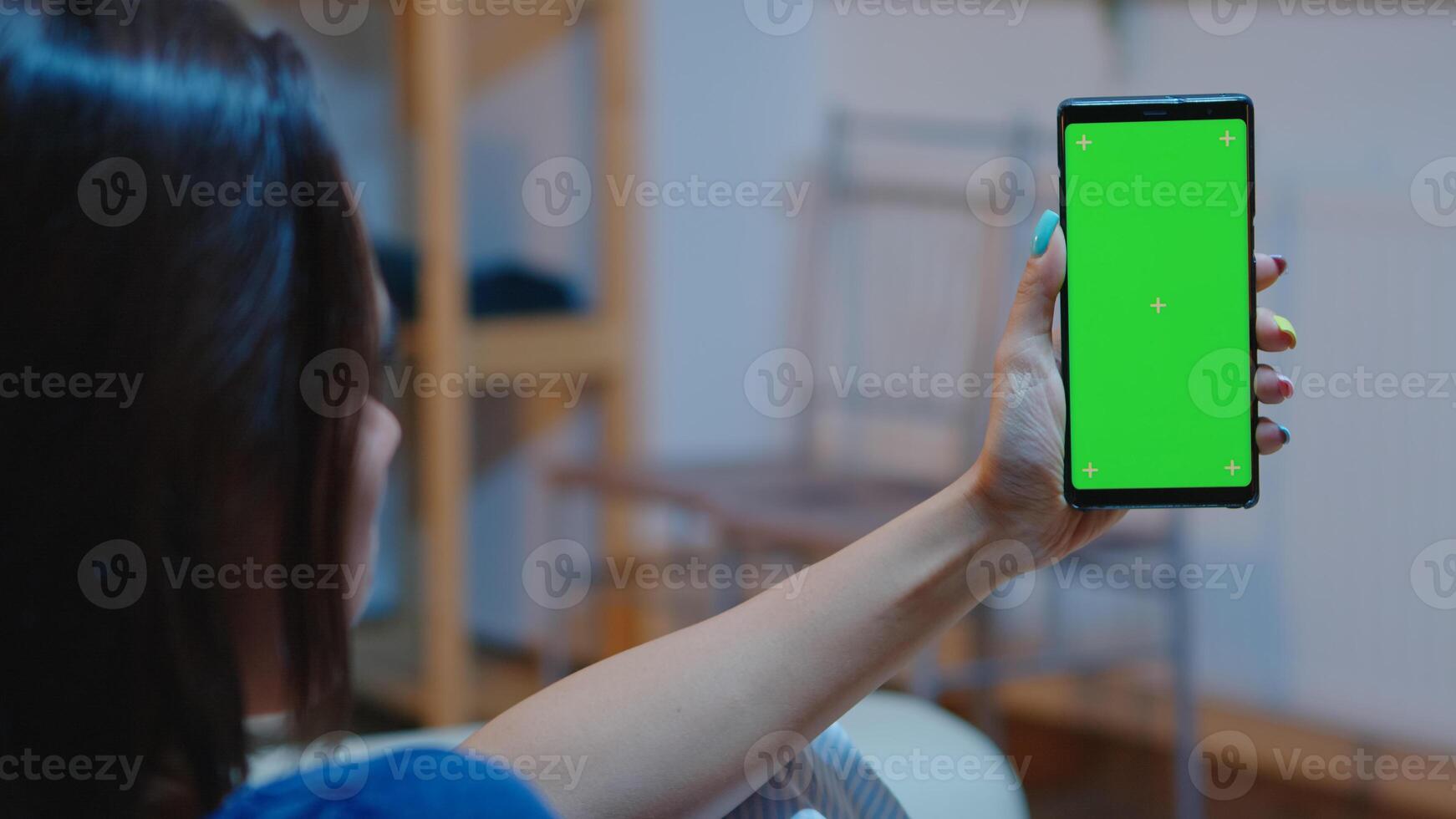 Housewife holding smartphone with chroma screen on hand looking at mockup. Reading on green screen template chroma key isolated mobile phone display using techology internet sitting on cozy couch photo