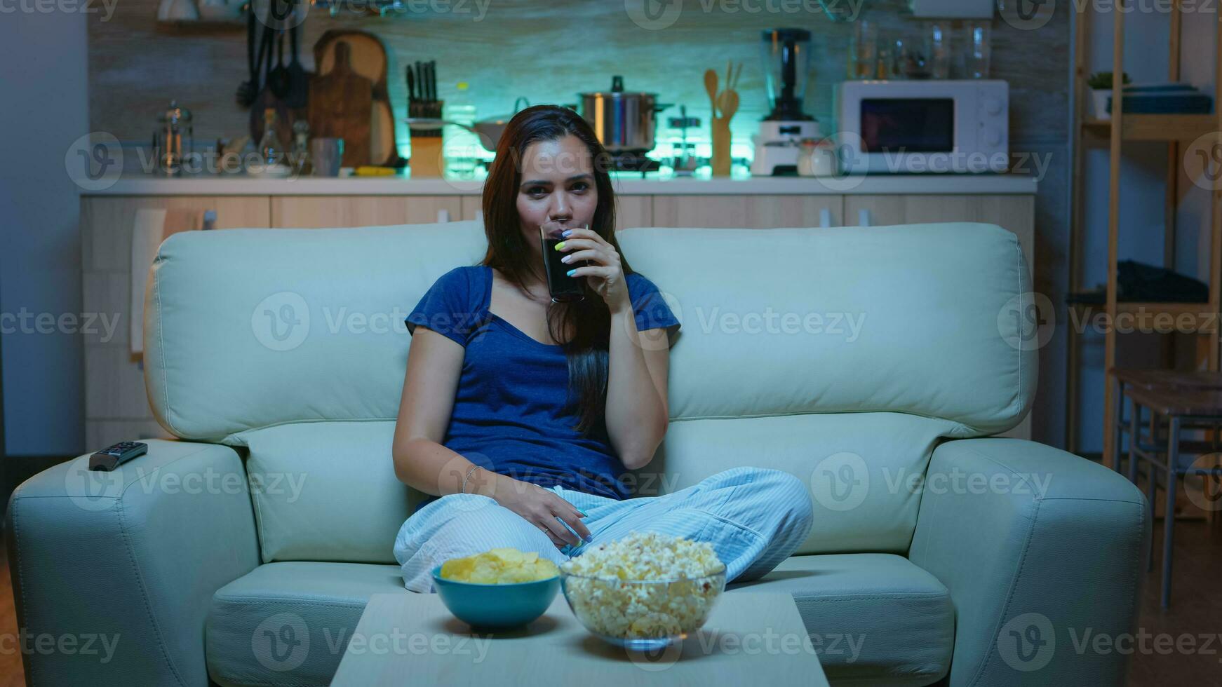 Happy woman spending her free time watching TV eating popcorn and drinking juice. Excited amused home alone lady enjoying the evening at home sitting on comfortable couch dressed in pajamas. photo