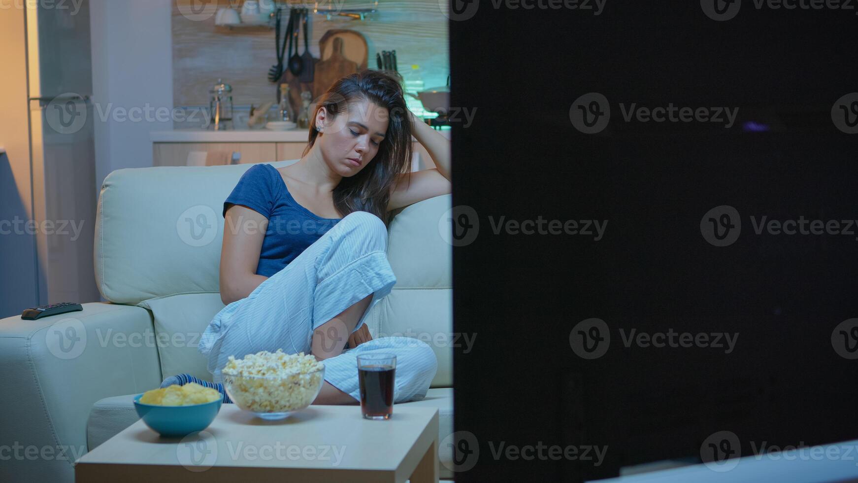 Caucasian woman falling asleep on sofa at home while watching TV. Tired exhausted lonely sleepy housewife in pajamas sleeping in front of television sitting on cozy couch in living room. photo