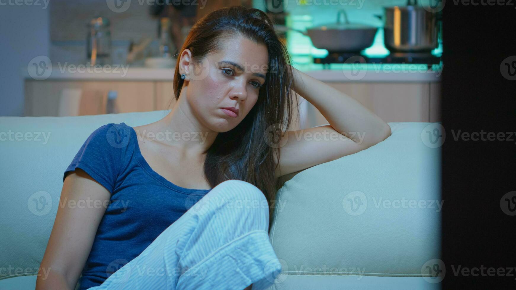 Tired woman closing eyes while watching movie at night. Tired exhausted lonely sleepy housewife in pajamas sleeping in front of television sitting on cozy couch in living room at home. photo