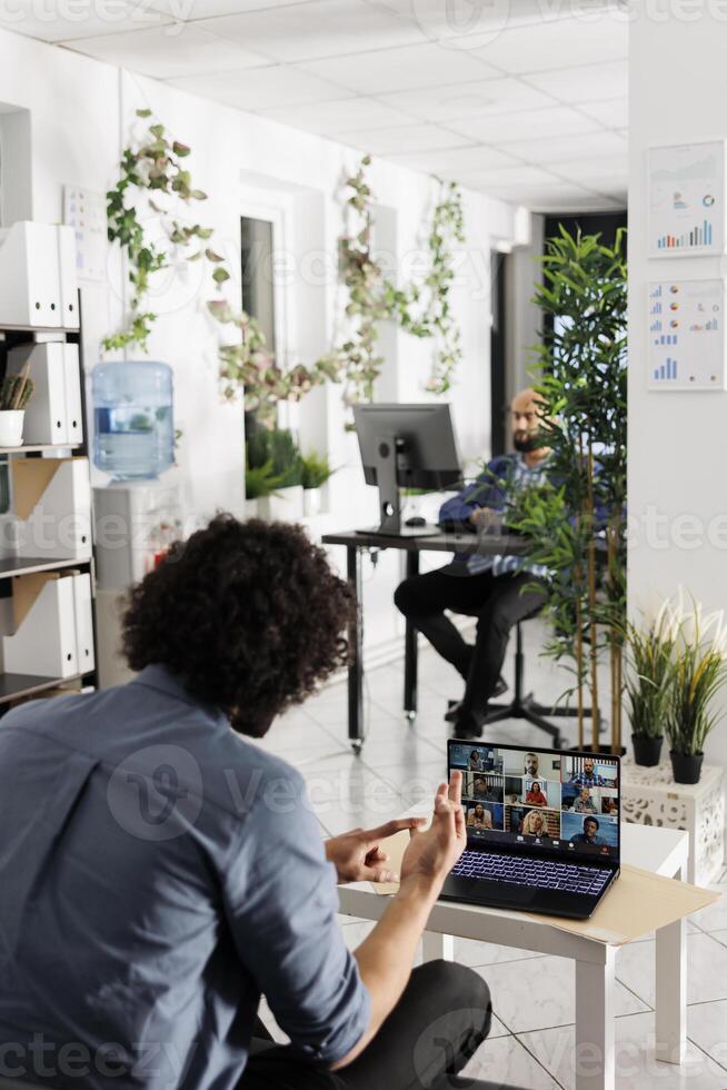 Project manager communicating with coworkers via video call to discuss work progress. Employees team talking about company growth strategy in online meeting using laptop in office photo
