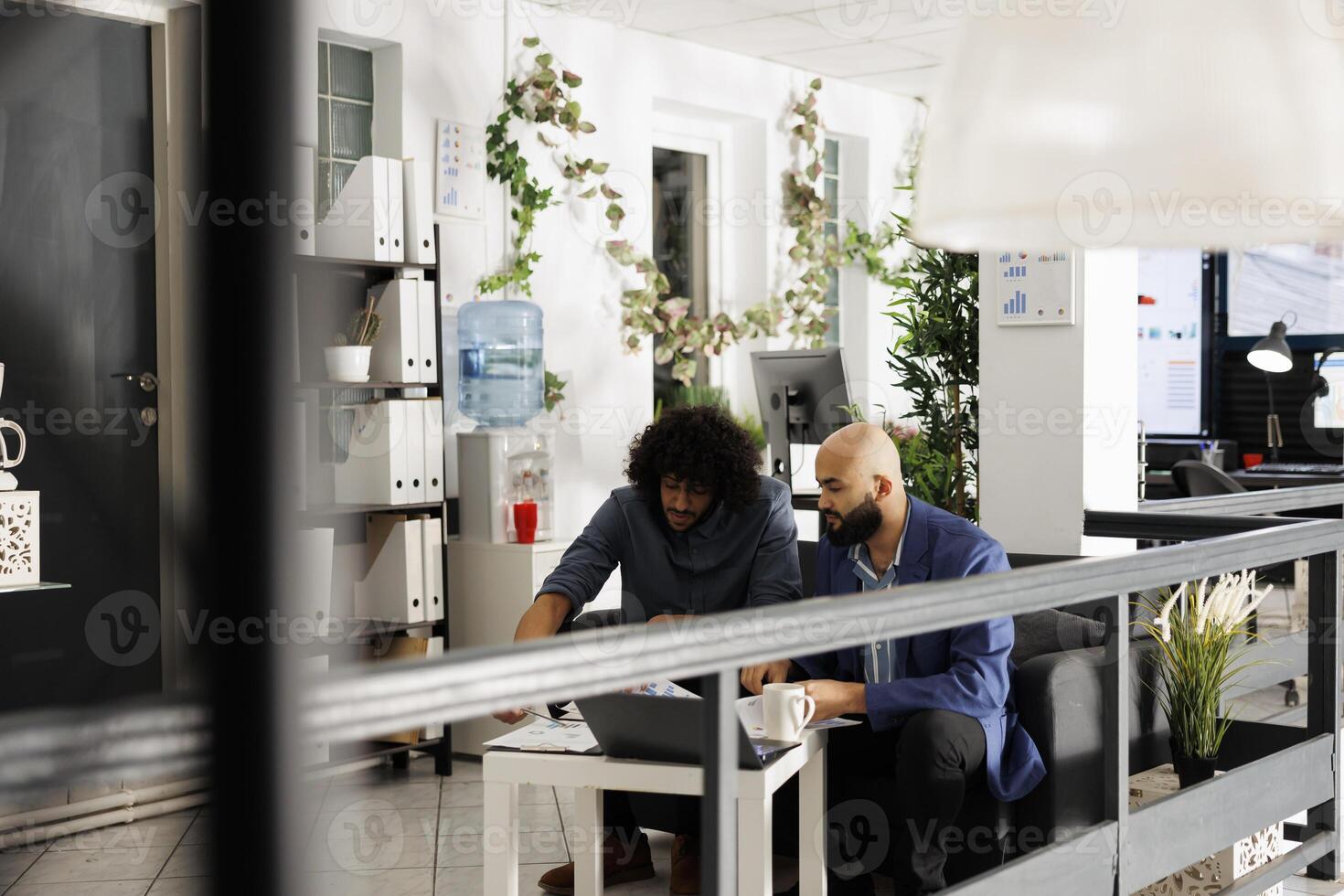 Startup team checking financial report on clipboard in business office workplace. Arab coworkers discussing project strategy while sitting on couch in green coworking space photo