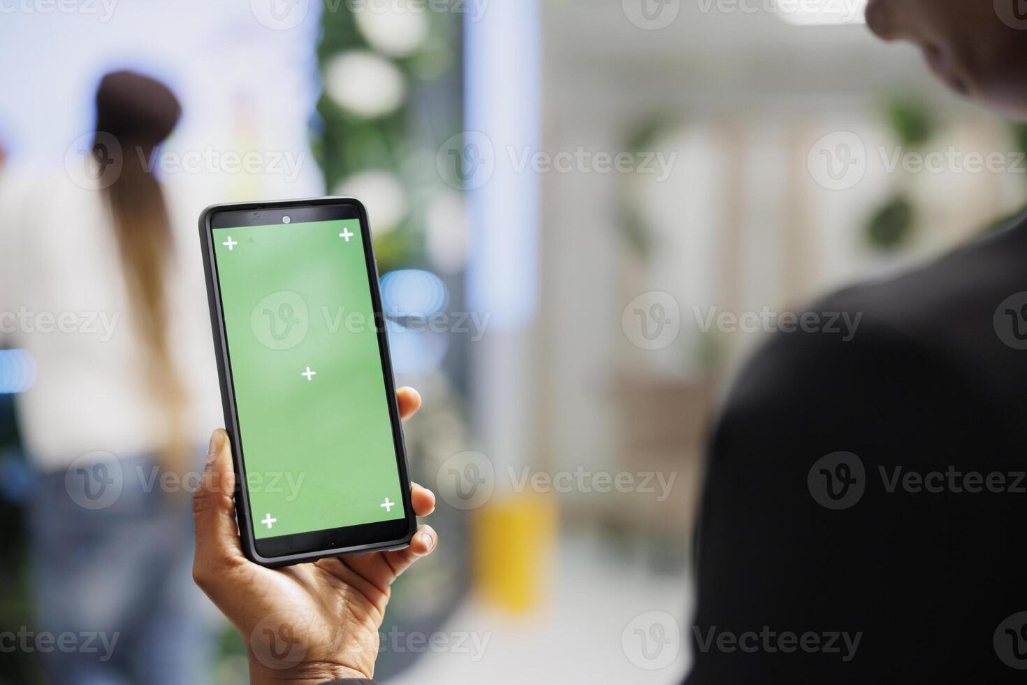 Customer using smartphone with green screen to check apparel reviews before buying clothes. African american woman holding mobile phone with chroma key display in shopping center photo