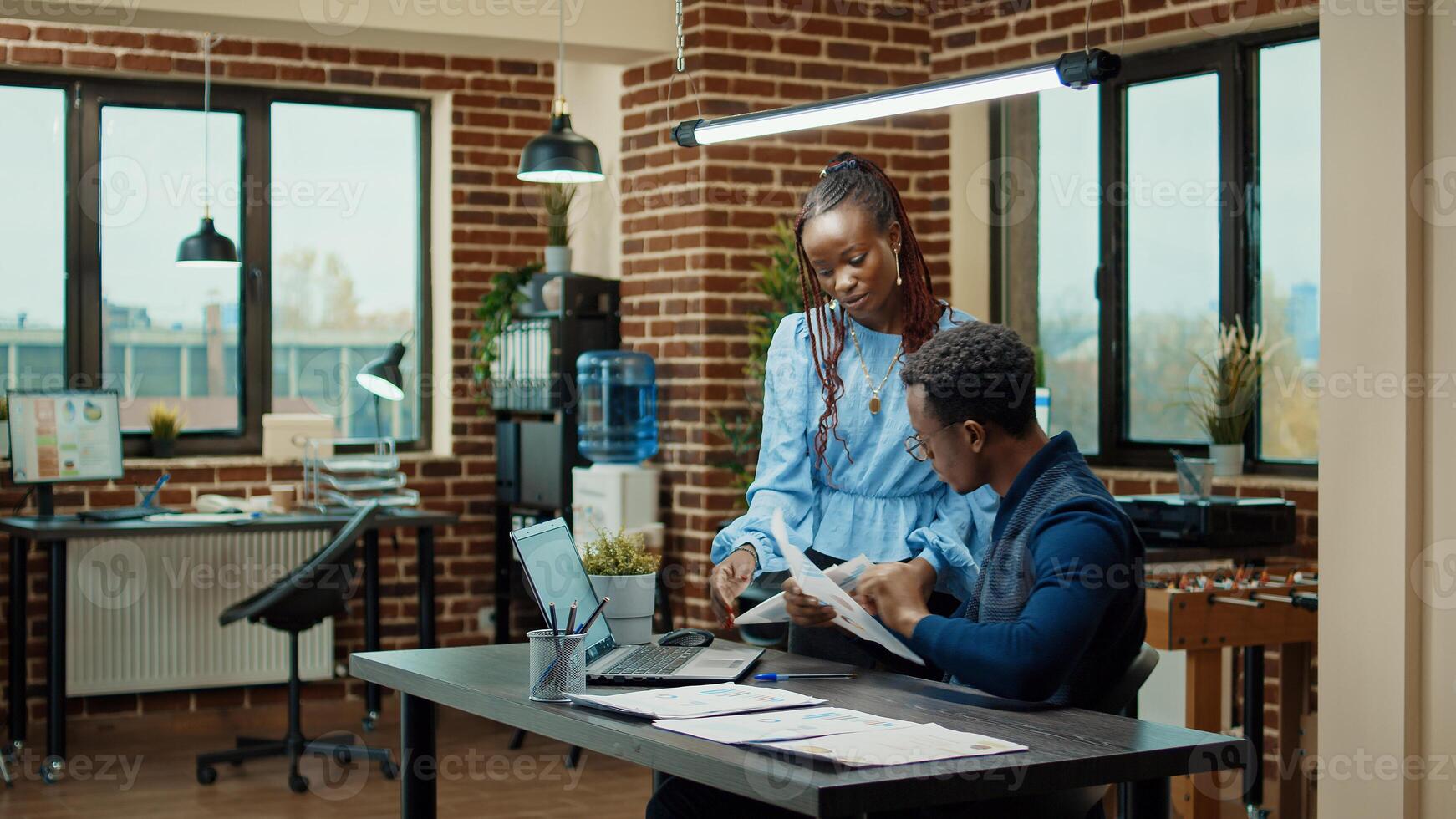 African american people planning report with annual data on papers and laptop, using online statistics to plan business development. Man and woman reviewing startup results in boardroom. photo