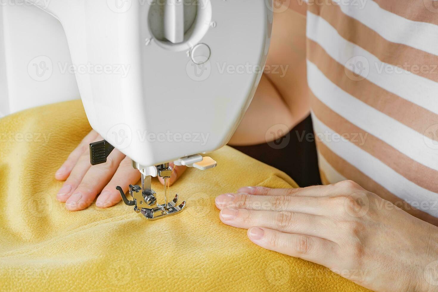 Tailor hands stitching yellow fabric on modern sewing machine at workplace in atelier photo