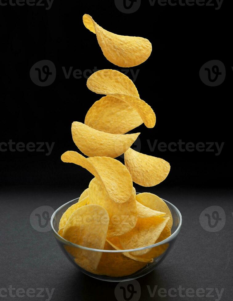 Potato chips falling into glass bowl on black background photo