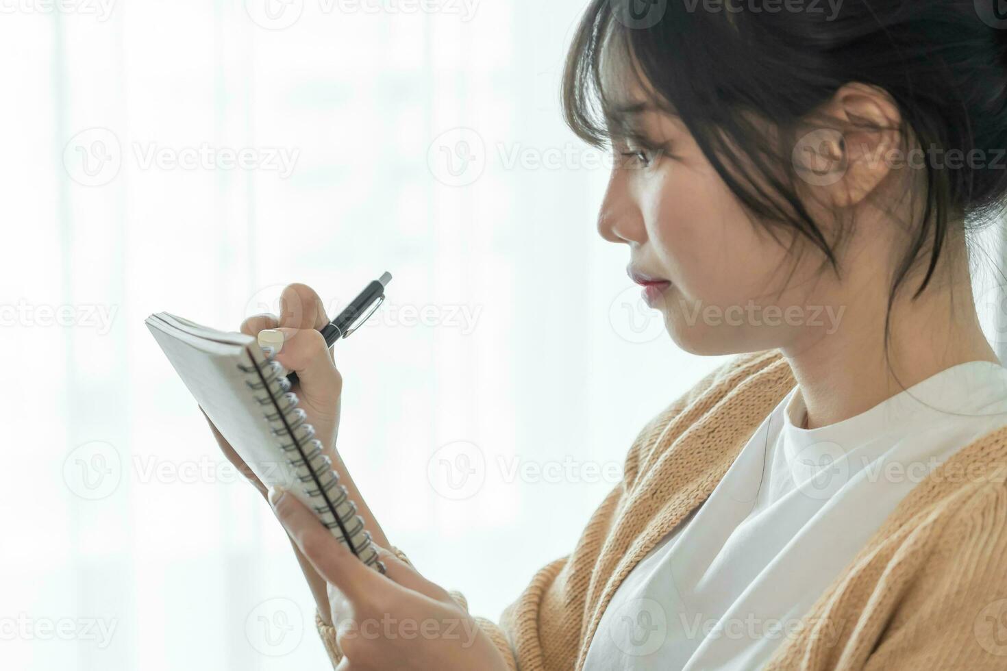 Asian Business woman working from office taking reading and writing notes in note pad photo