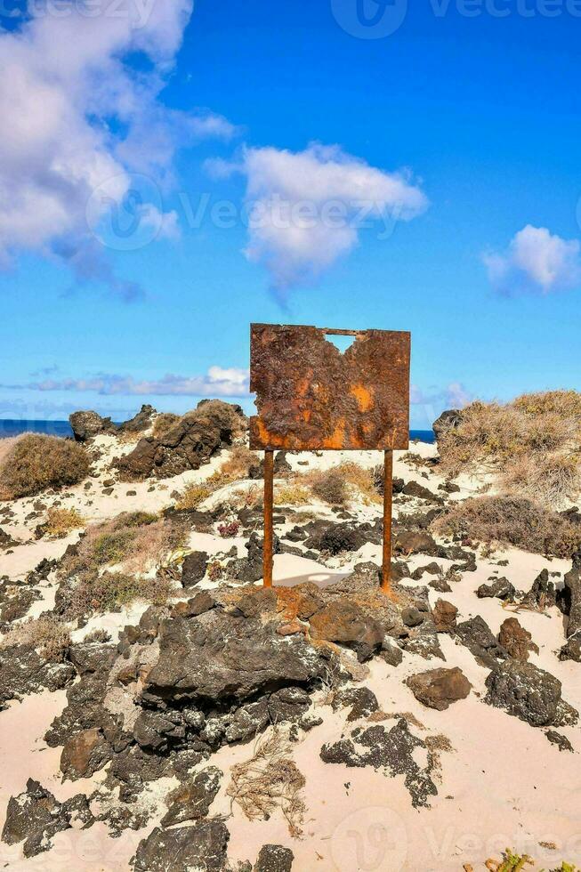 a rusty sign on the beach near the ocean photo