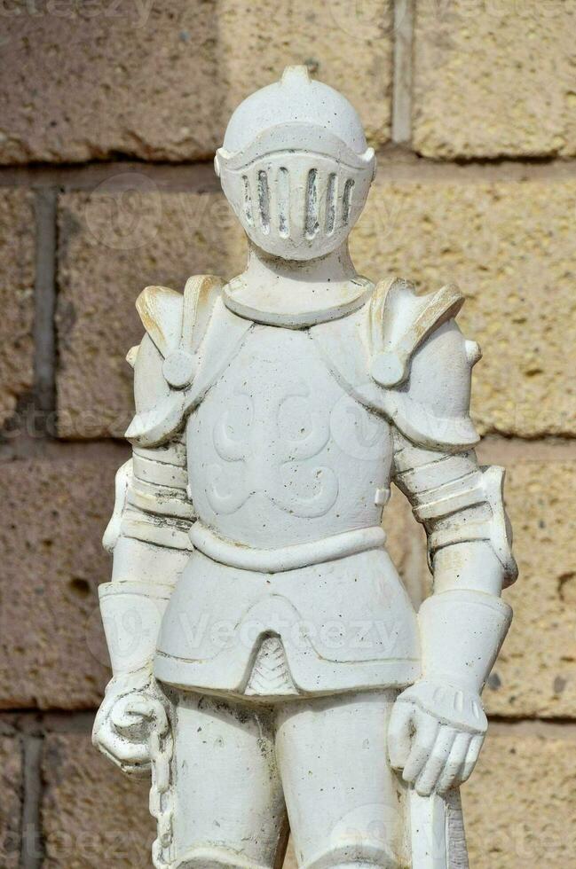 a statue of a knight in armor standing next to a brick wall photo