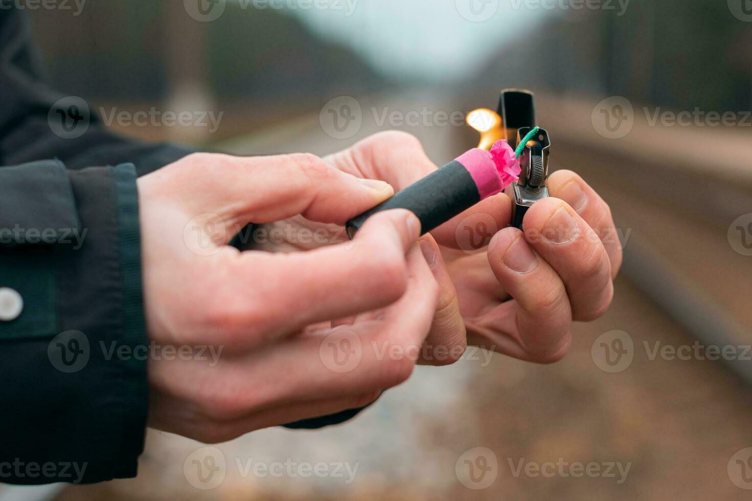 Setting Fire to the Firecracker. Man in Black Clothes Lighting Up the Petard. Firing Up the Pyrotechnics with a Black Gasoline Lighter Outdoors photo
