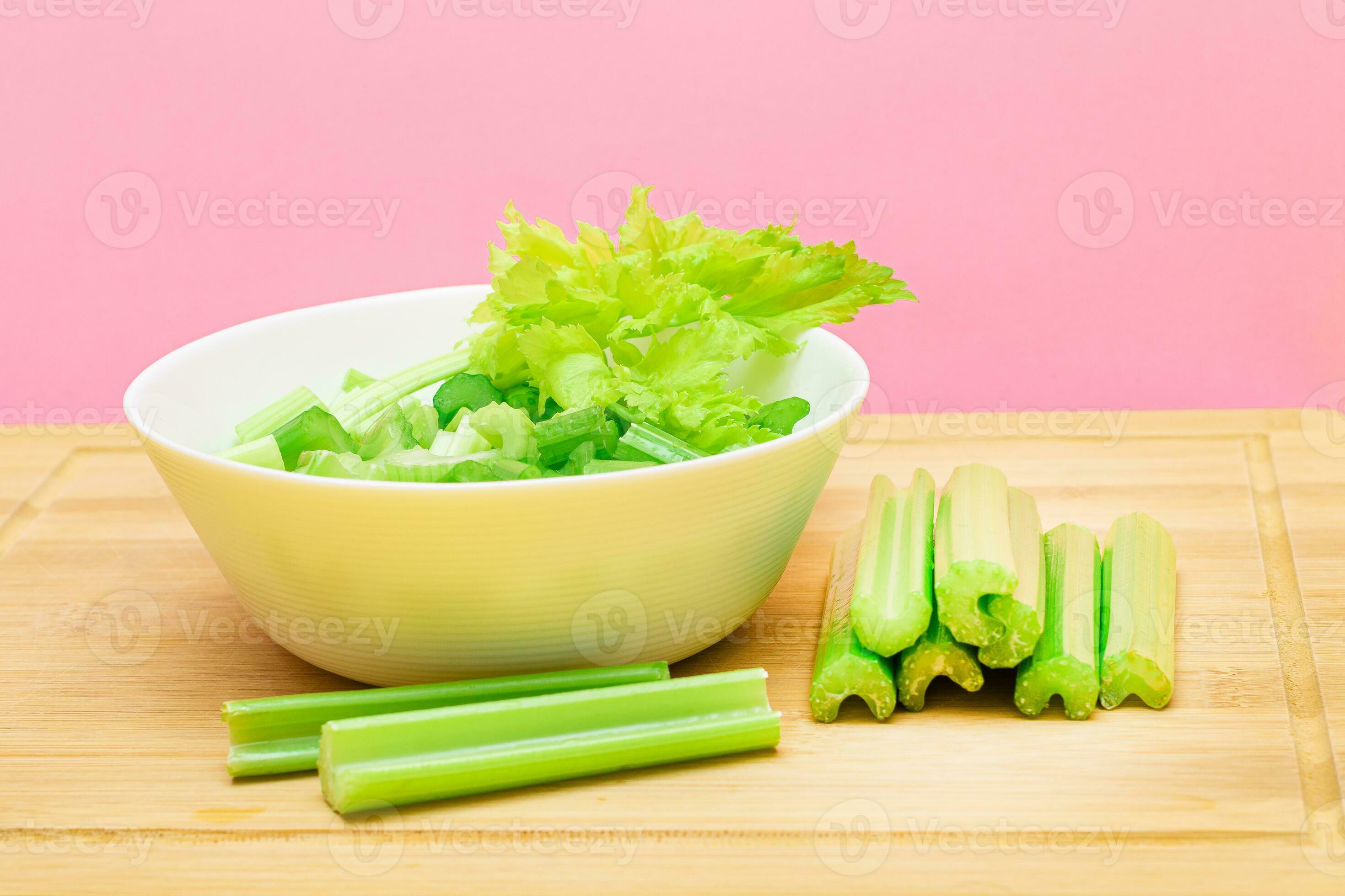 Fresh Chopped Celery Slices in White Bowl with Celery Sticks on Bamboo