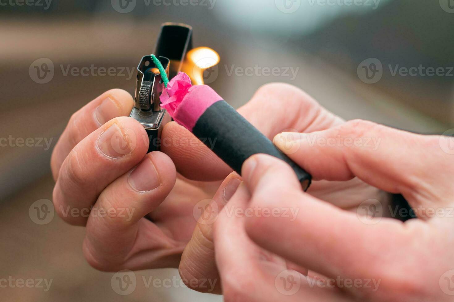 Setting Fire to the Firecracker. Man in Black Clothes Lighting Up the Petard. Firing Up the Pyrotechnics with a Black Gasoline Lighter Outdoors photo