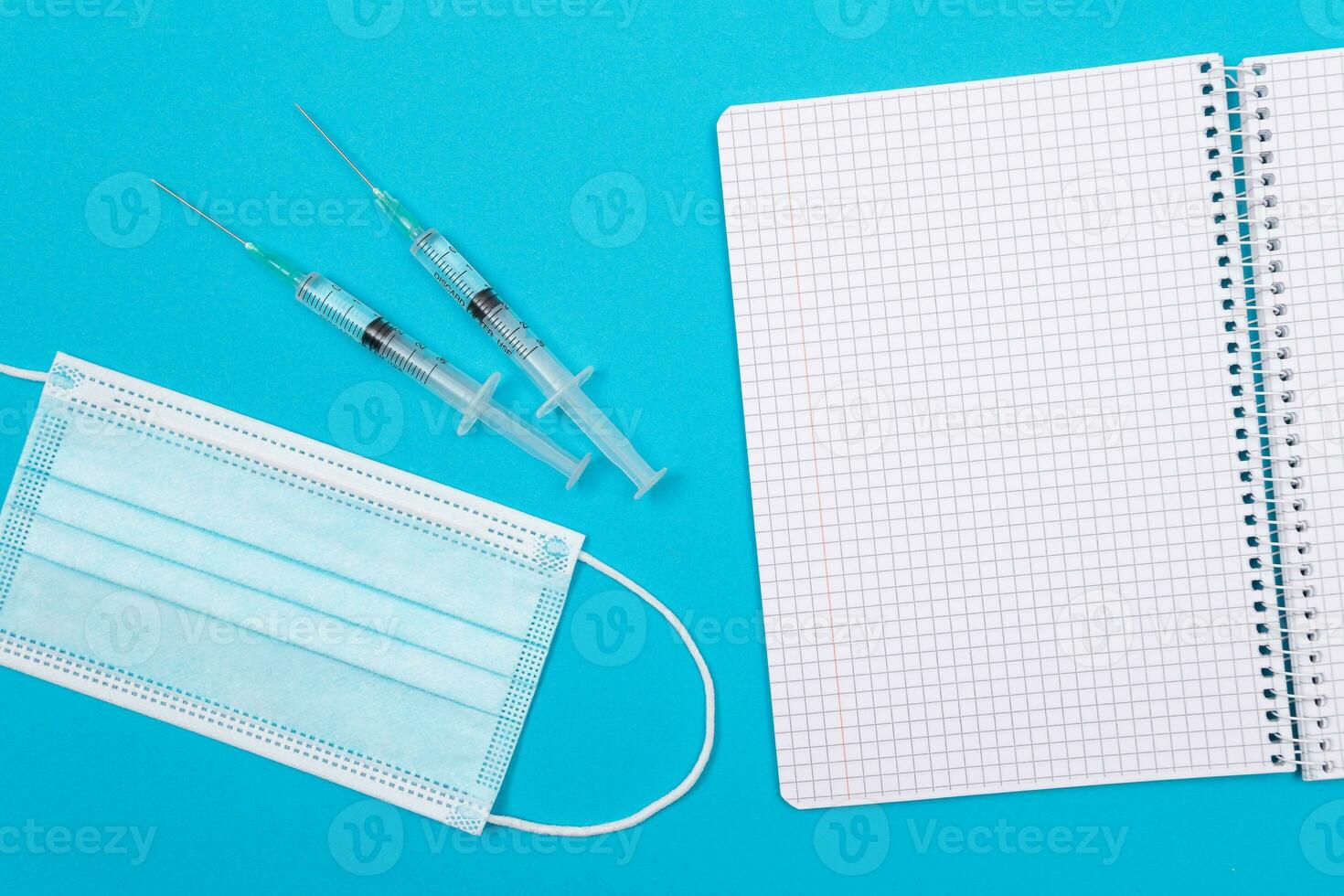 Vaccination, Immunology or Revaccination Concept Two Medical Syringe Lying on Blue Table in Doctor's Office in a Hospital or Clinic. Opened Blank Notepad Mock Up with Copy Space photo