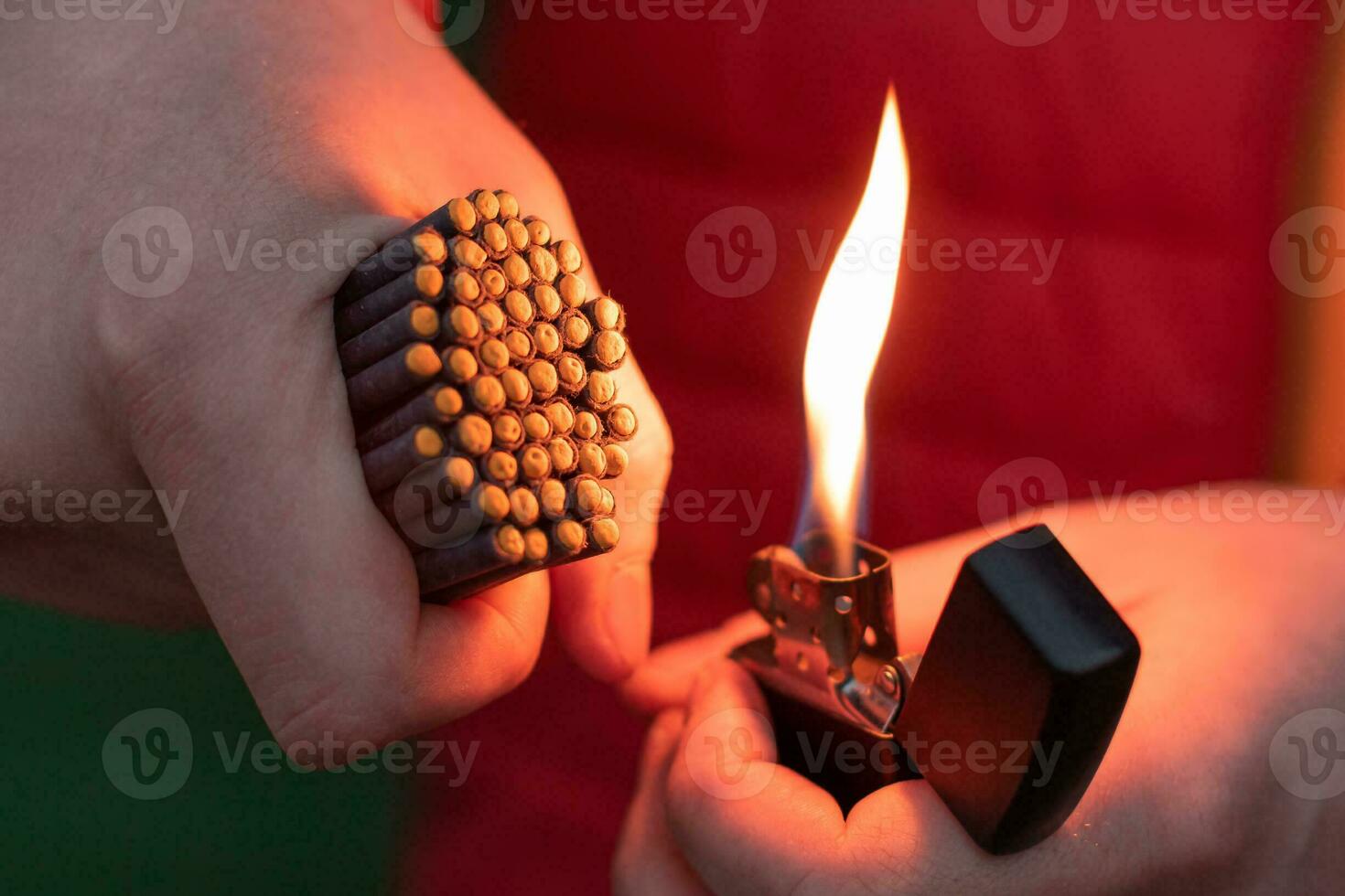 Man in Red Jacked Lighting Up Many Small Black Firecrackers in his Hand Using Gasoline Lighter. Guy Getting Ready for New Year Fun with Fireworks or Pyrotechnic Products photo