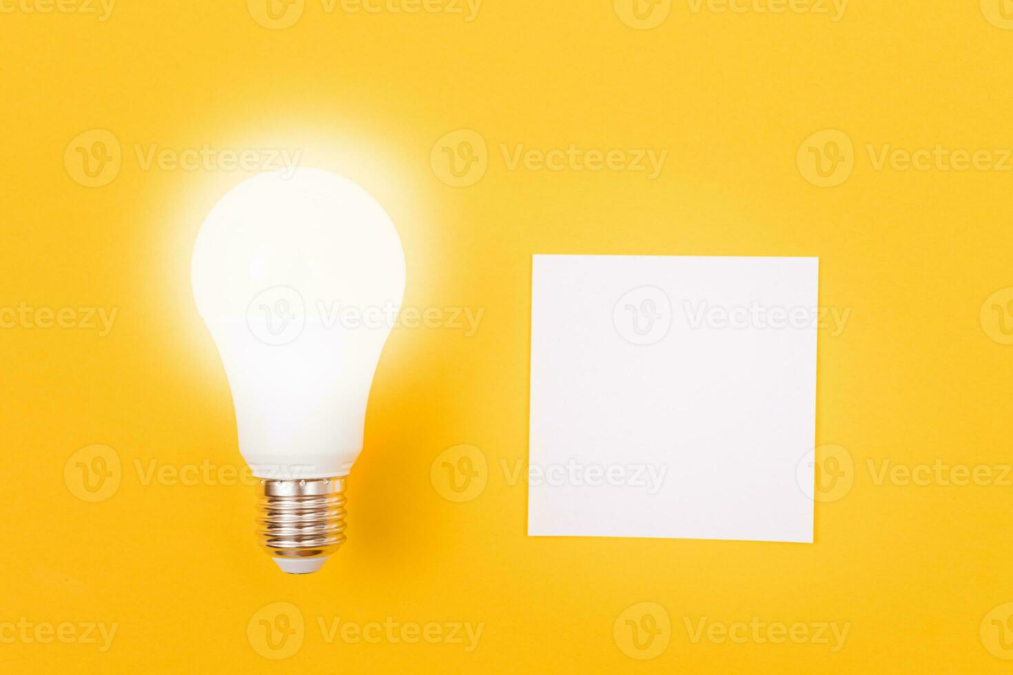 A Power Saving Lamp with White Note Paper Lying on Yellow Table, Blank Template with Copy Space Top View, Flat Lay photo