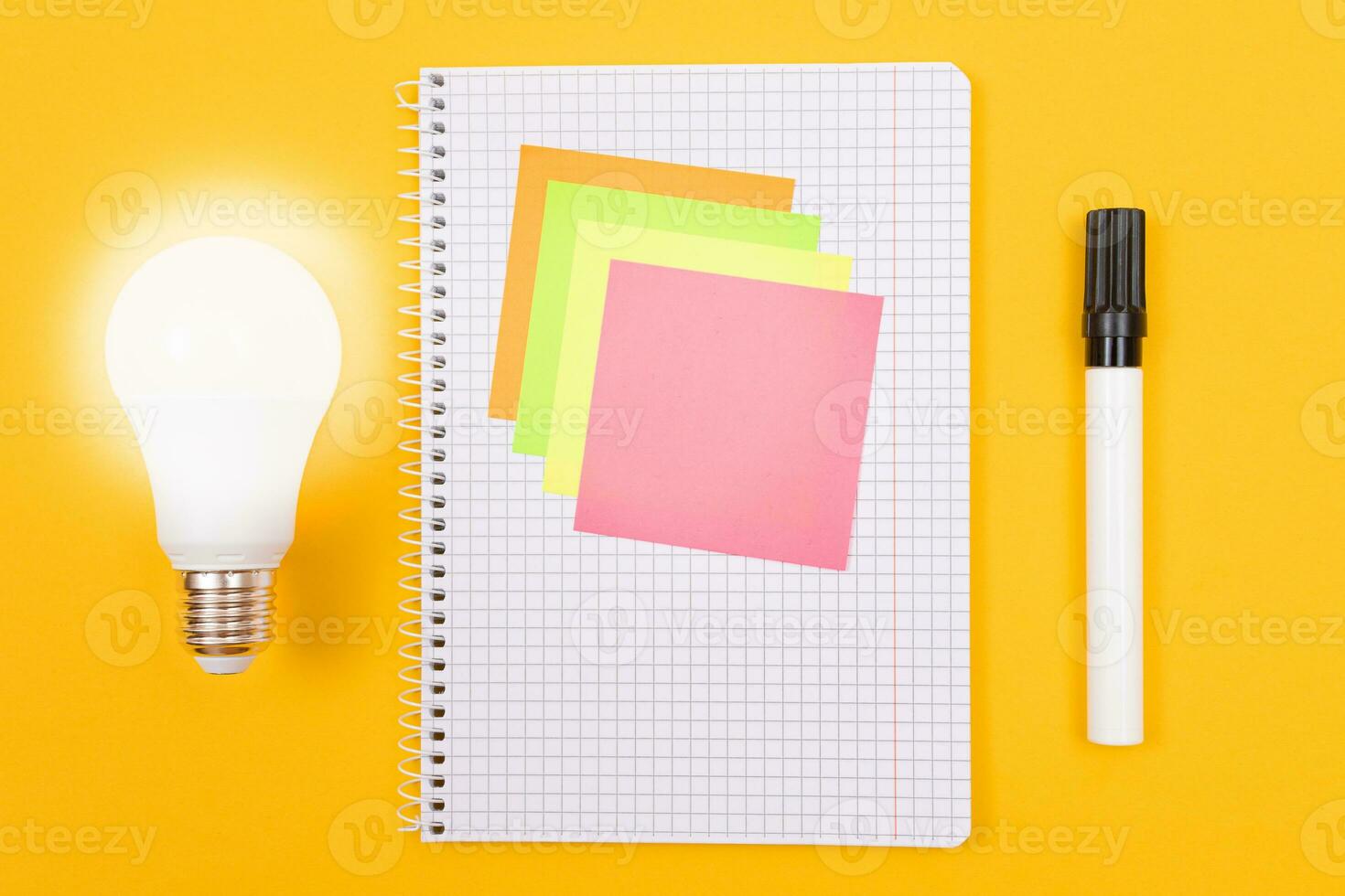 Glowing Power Saving Lamp and Notepad with Sticky Notes Lying on Yellow Table, Blank Template with Copy Space Top View, Flat Lay photo