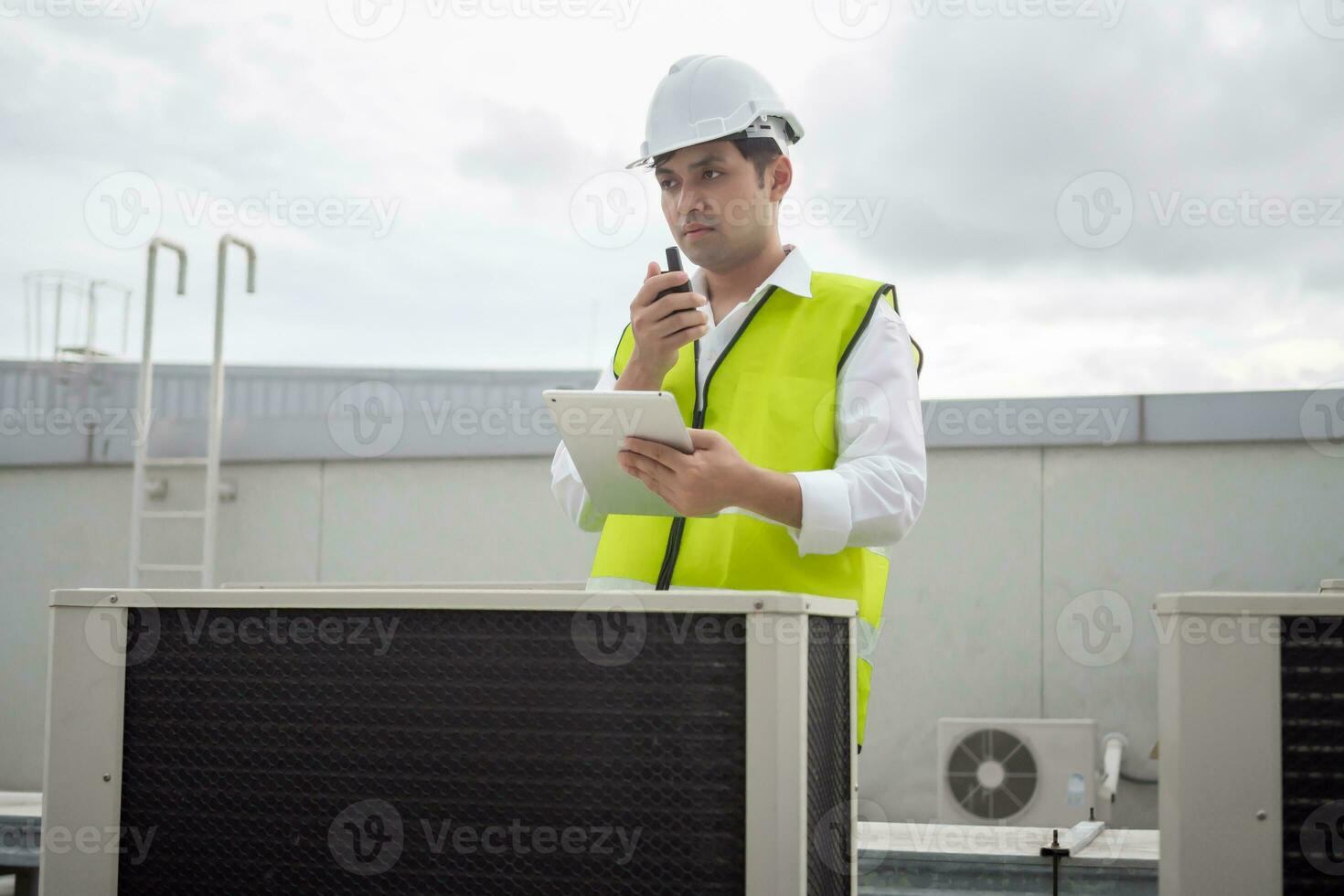 Asian maintenance engineer works on the roof of factory. contractor inspect compressor system and plans installation of air condition systems in construction. technology, online, mobile application. photo