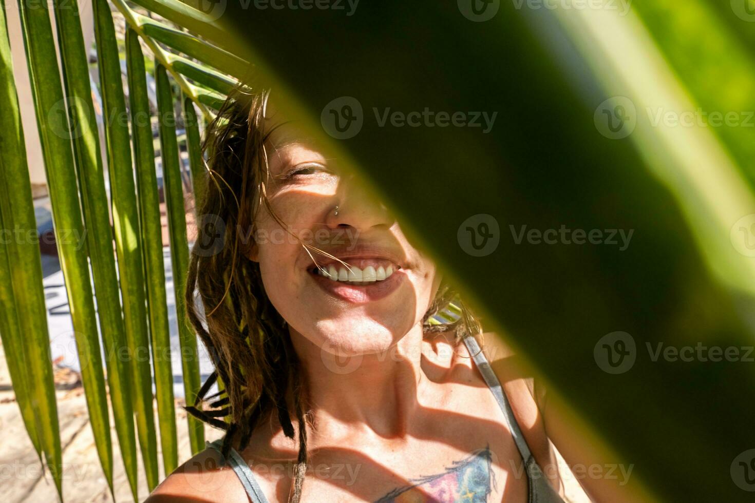 Smiling woman taking selfie under palm leaf on tropical beach. Summery vacations moment. photo