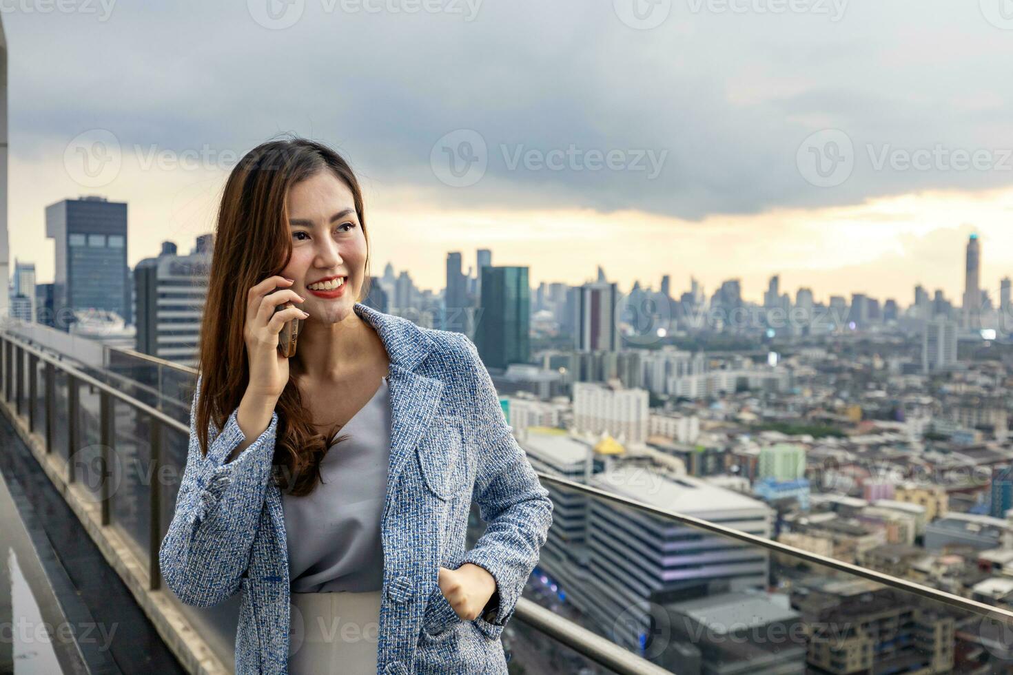 Asian business woman in formal suit is phone calling customer while standing outside the skyscraper building for marketing, connection, corporate work, real estate, housing and urban development photo