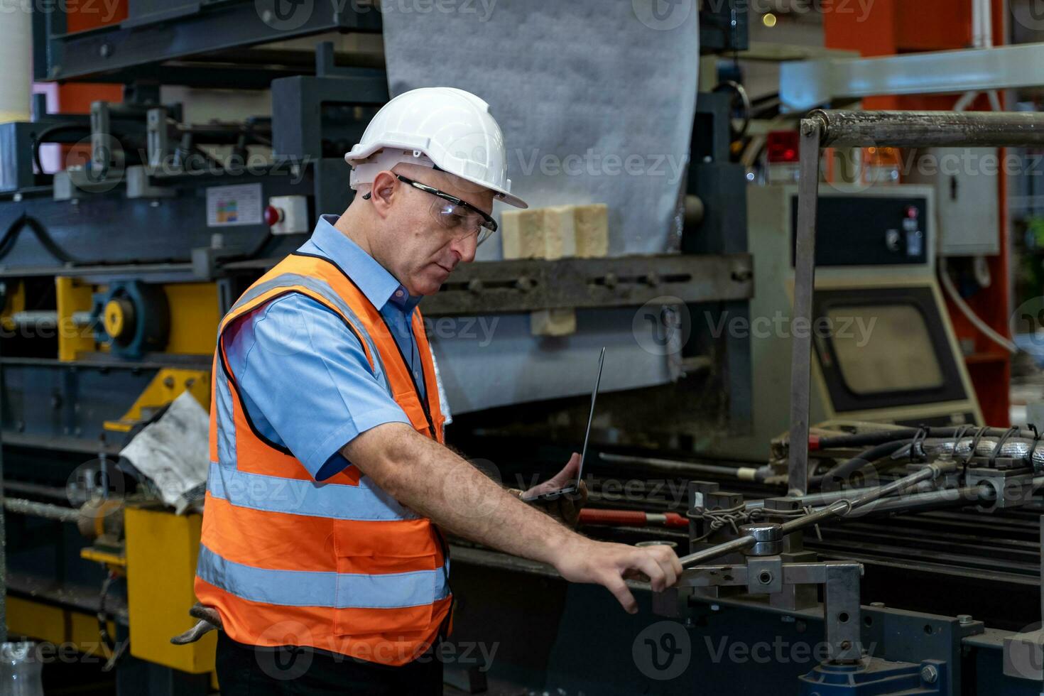 Caucasian industrial worker is using laptop computer to calibrating the machine while inspecting inside the metal sheet galvanized roof factory for safety industry photo