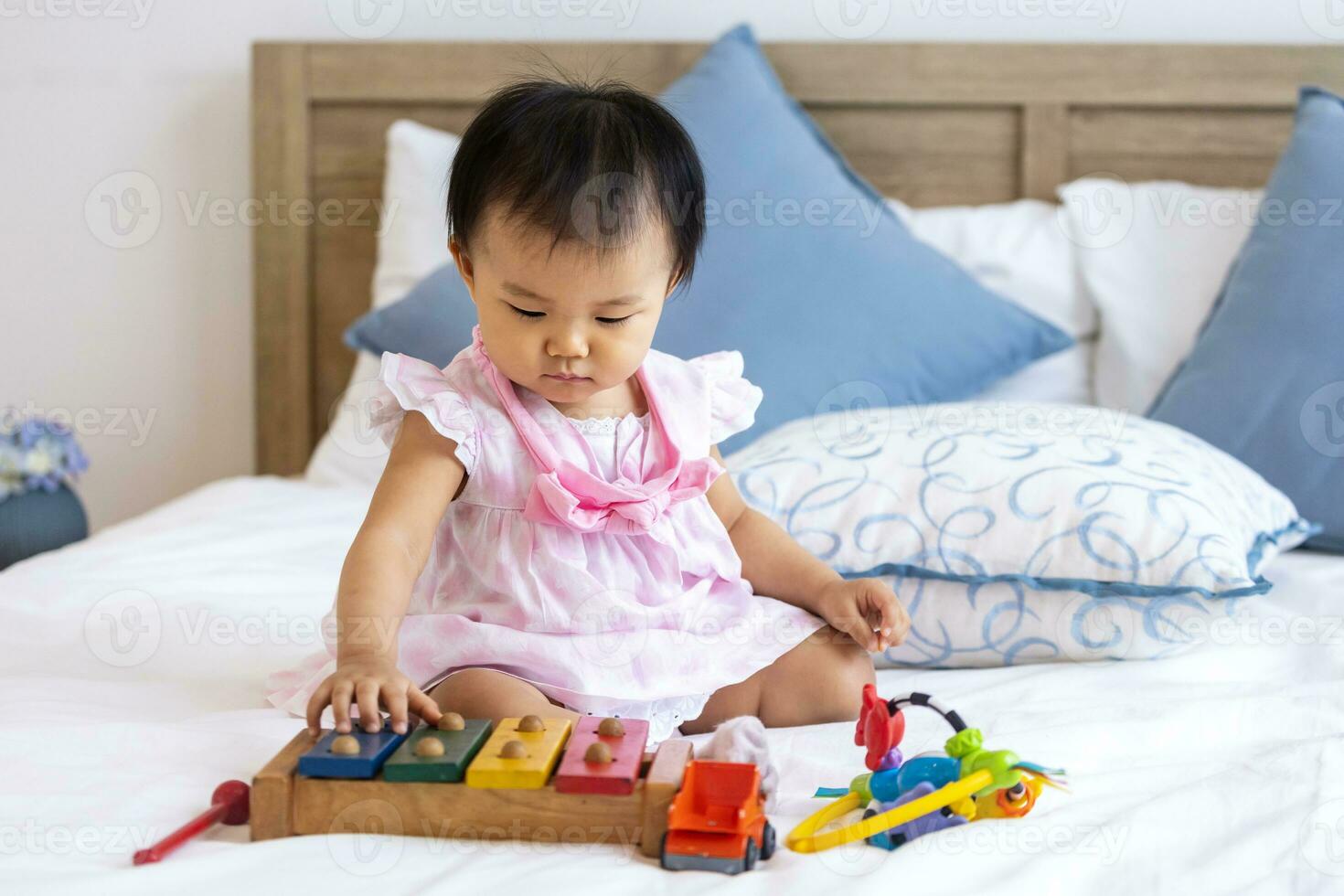 adorable pequeño asiático bebé niñito es sentado en el cama jugando de madera melodía juguete para preescolar aprendizaje y crecimiento desarrollo concepto foto