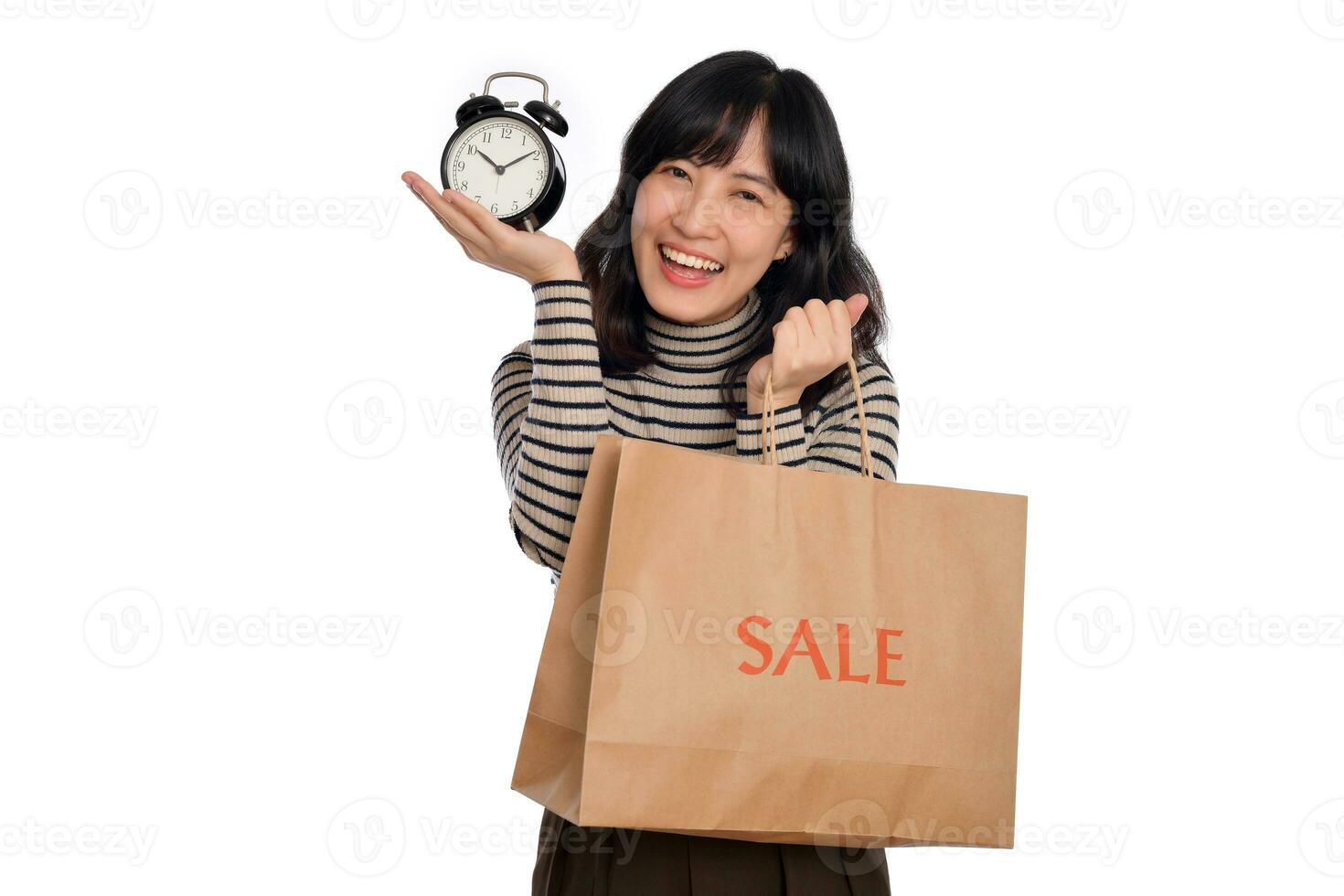 retrato de contento joven asiático mujer con suéter camisa participación alarma reloj y compras papel espalda aislado en blanco antecedentes foto