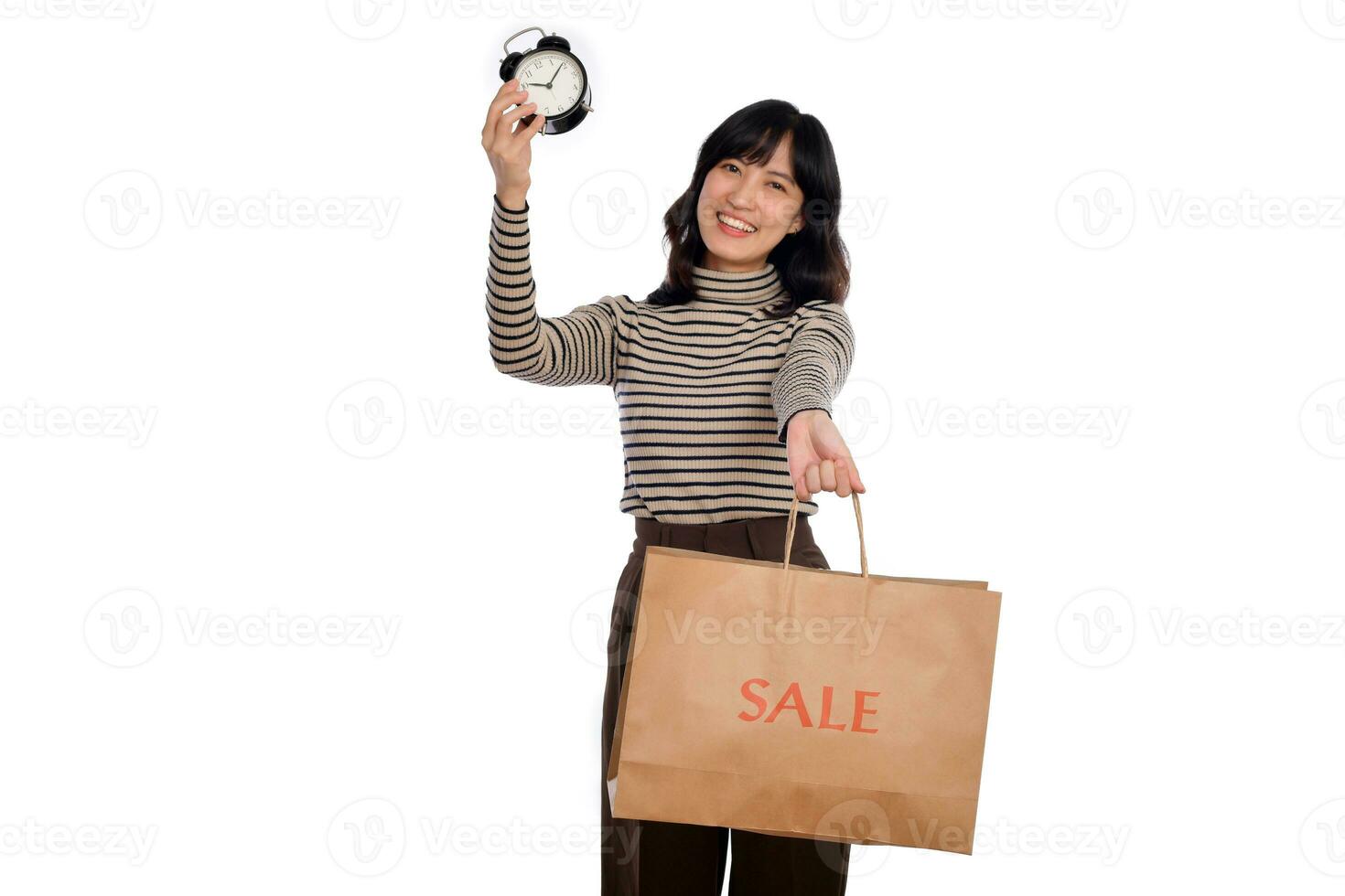 retrato de contento joven asiático mujer con suéter camisa participación alarma reloj y compras papel espalda aislado en blanco antecedentes foto