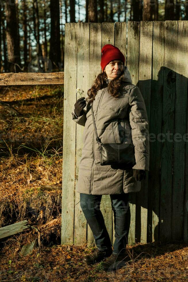 Middle-Aged Woman Strikes a Pose in Stylish Fall Outfit by Weathered Fence on Sunny Autumn Day photo