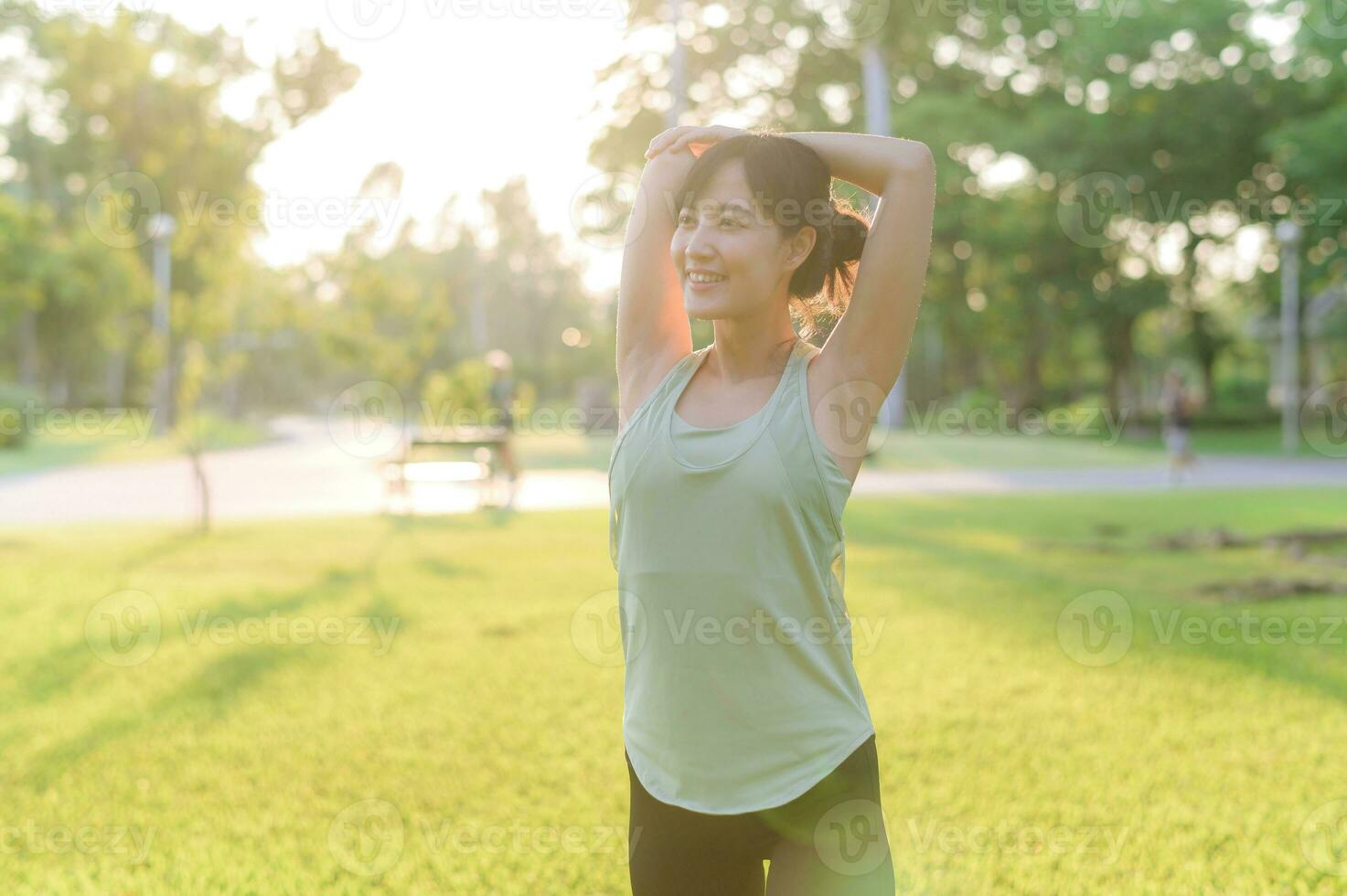 Female jogger. Fit young Asian woman with green sportswear stretching muscle in park before running and enjoying a healthy outdoor. Fitness runner girl in public park. Wellness being concept photo