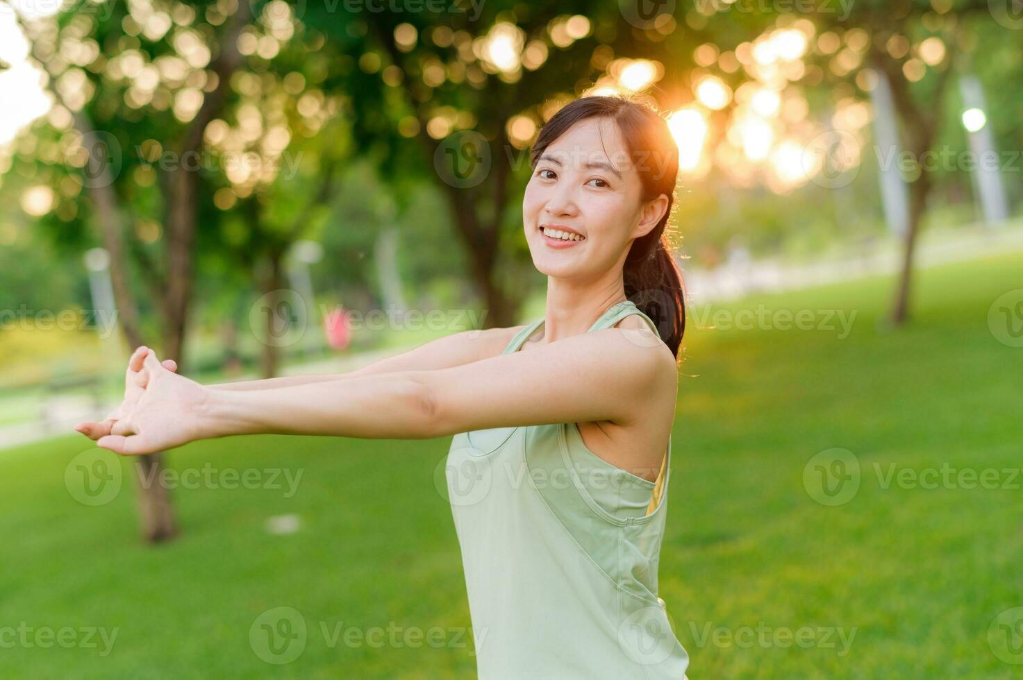 Female jogger. Fit young Asian woman with green sportswear stretching muscle in park before running and enjoying a healthy outdoor. Fitness runner girl in public park. Wellness being concept photo