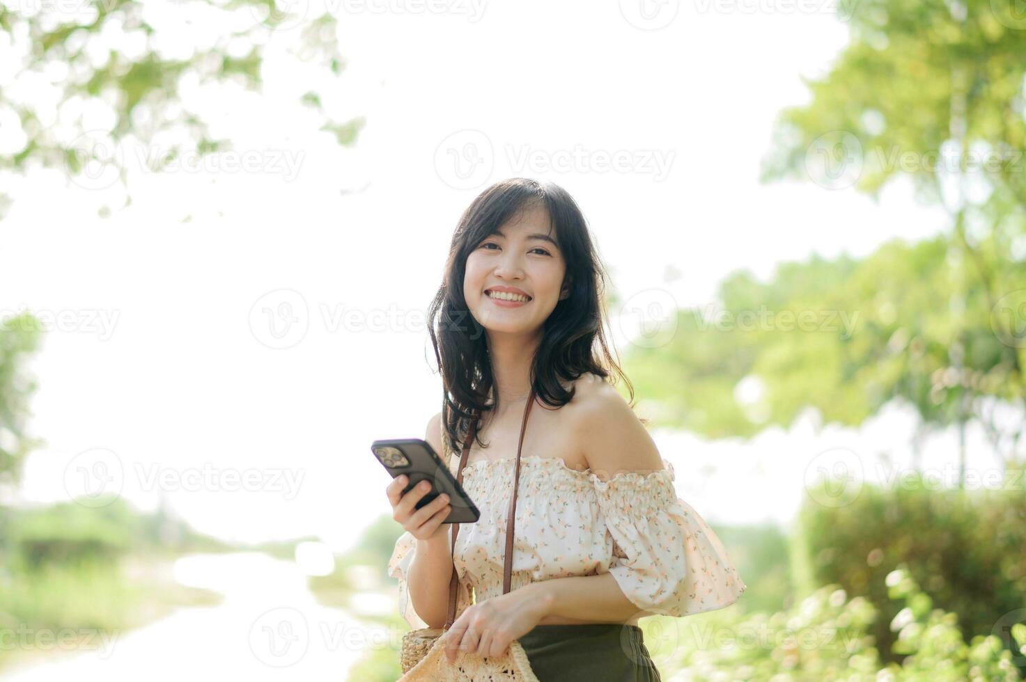 Portrait of asian young woman traveler with weaving hat, basket, mobile phone and camera on green public park background. Journey trip lifestyle, world travel explorer or Asia summer tourism concept. photo
