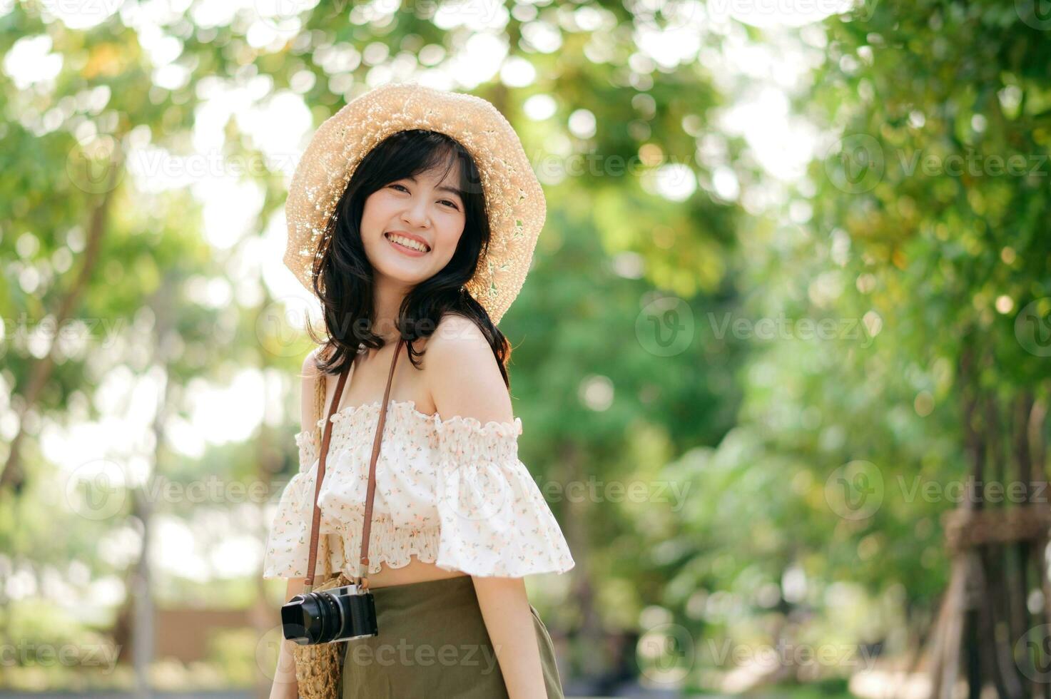 Portrait of asian young woman traveler with weaving hat and basket and a camera on green public park nature background. Journey trip lifestyle, world travel explorer or Asia summer tourism concept. photo