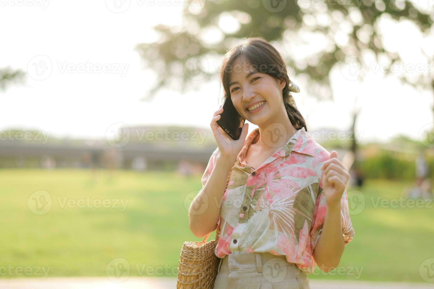 Portrait of asian young woman traveler with weaving basket, mobile phone on green public park background. Journey trip lifestyle, world travel explorer or Asia summer tourism concept. photo