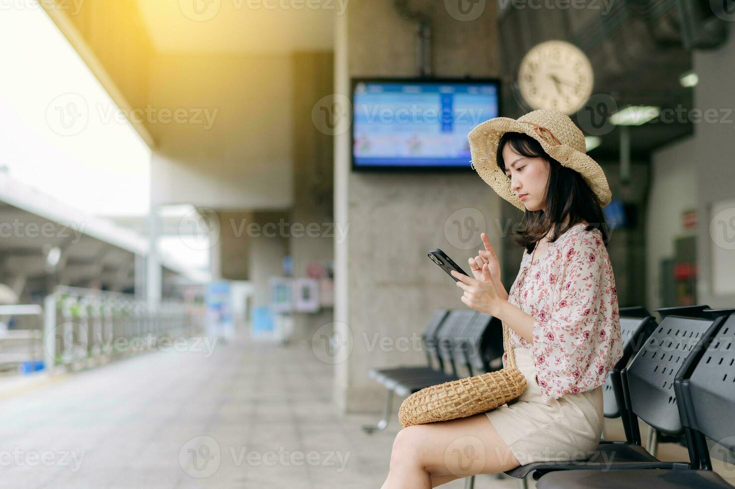 young asian woman traveler with weaving basket using a mobile phone and waiting for train in train station. Journey trip lifestyle, world travel explorer or Asia summer tourism concept. photo