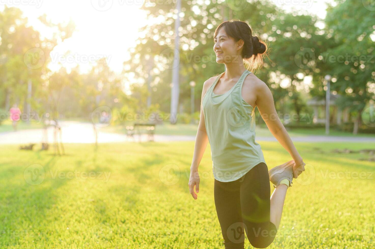 Female jogger. Fit young Asian woman with green sportswear stretching muscle in park before running and enjoying a healthy outdoor. Fitness runner girl in public park. Wellness being concept photo