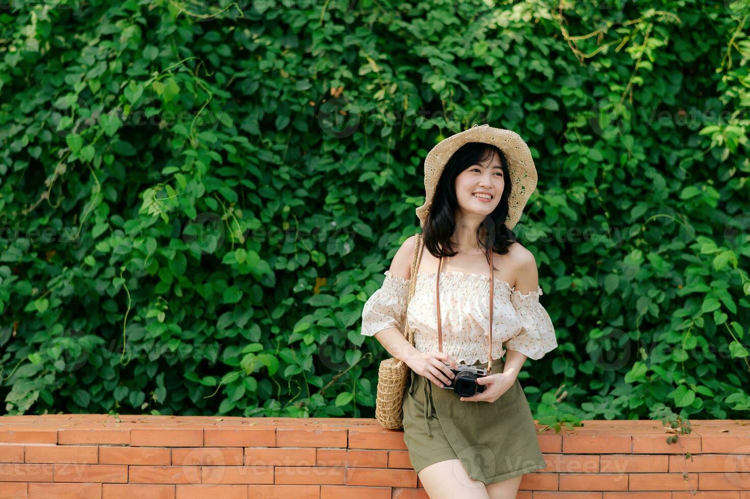 Portrait of asian young woman traveler with weaving hat and basket and a camera on green public park nature background. Journey trip lifestyle, world travel explorer or Asia summer tourism concept. photo