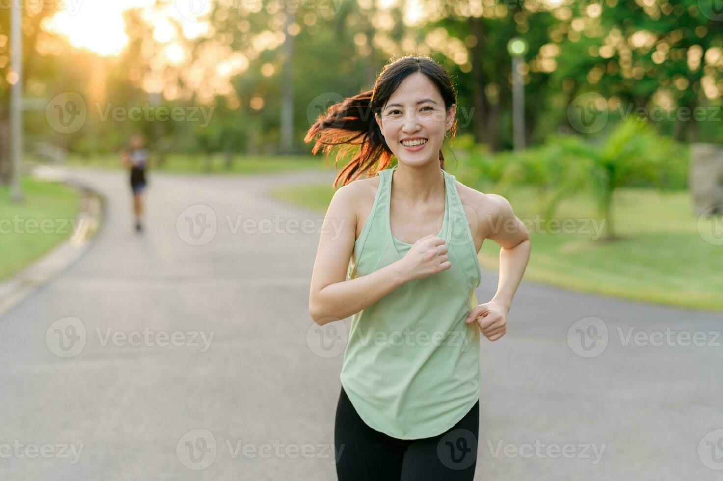 Fit Asian young woman jogging in park smiling happy running and enjoying a healthy outdoor lifestyle. Female jogger. Fitness runner girl in public park. healthy lifestyle and wellness being concept photo