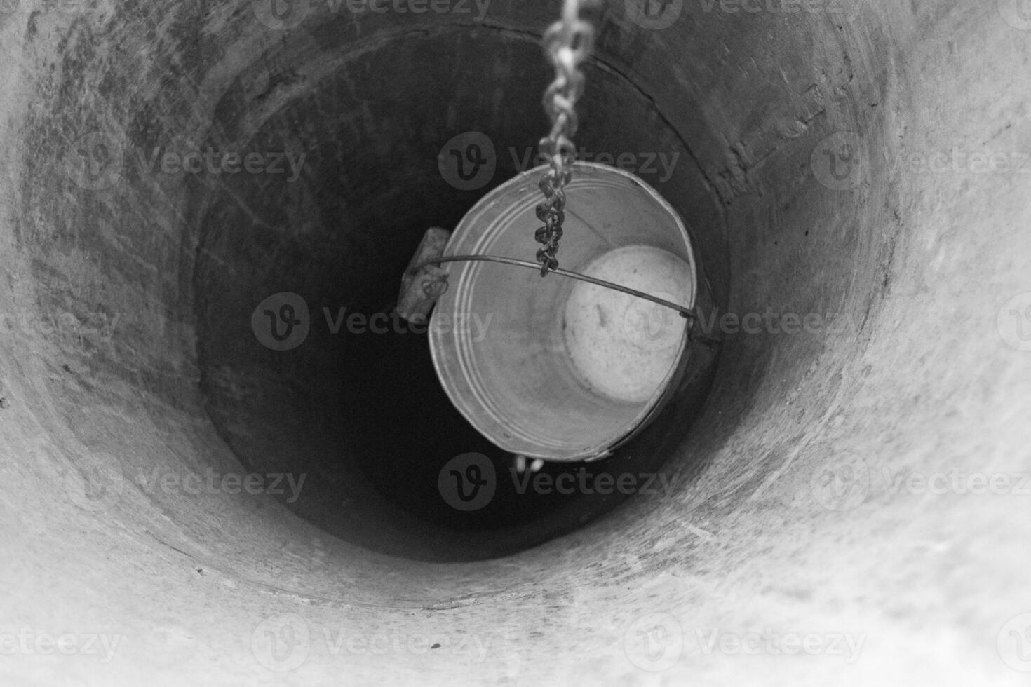 Old well with iron bucket on long forged chain for clean drinking water photo