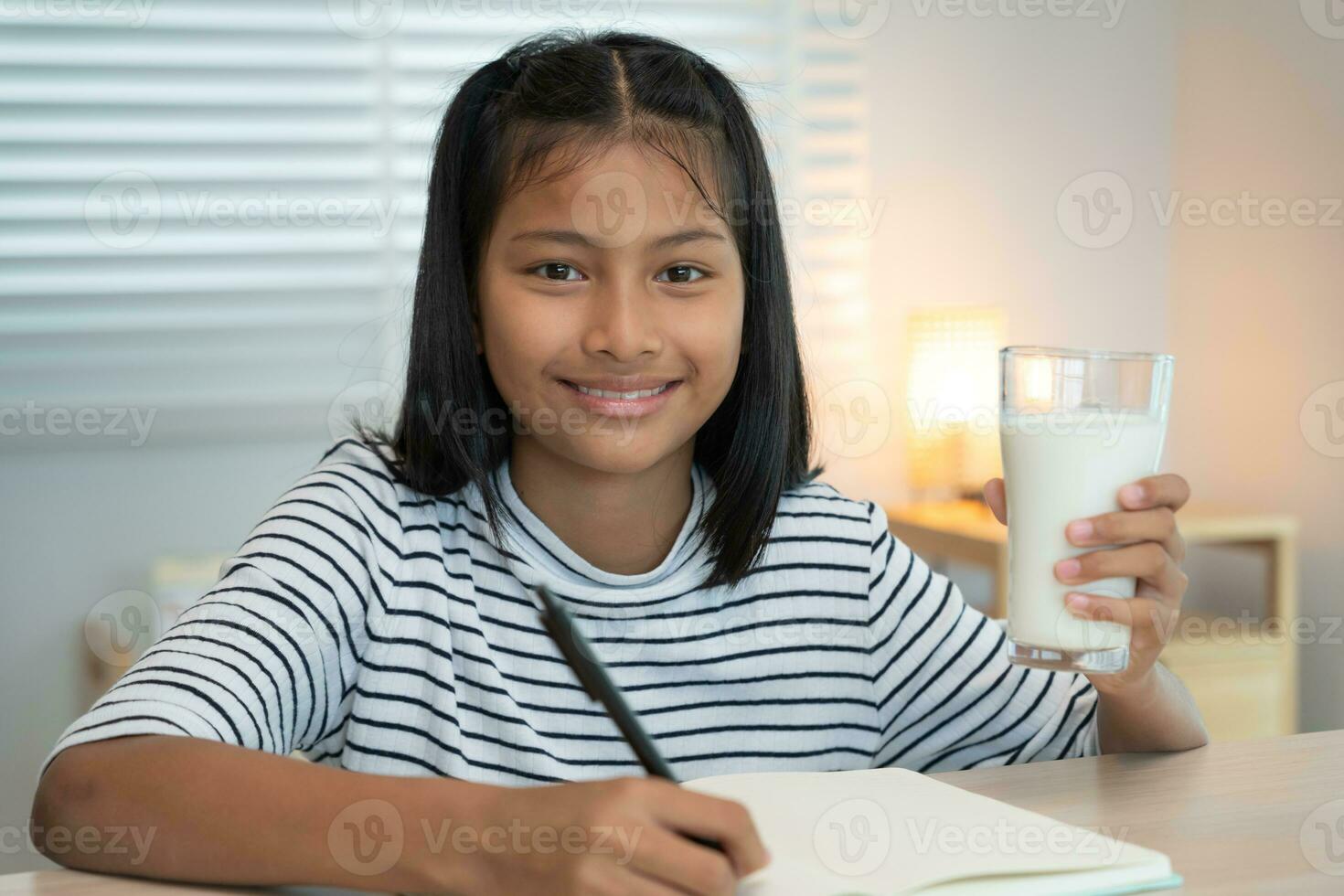 los niños las mujeres beben leche para nutrir el cuerpo y nutrir el cerebro. una niña asiática aprende en casa. niña feliz bebe leche y lee un libro para el examen, educación en el hogar. educación, vitaminas, desarrollo foto