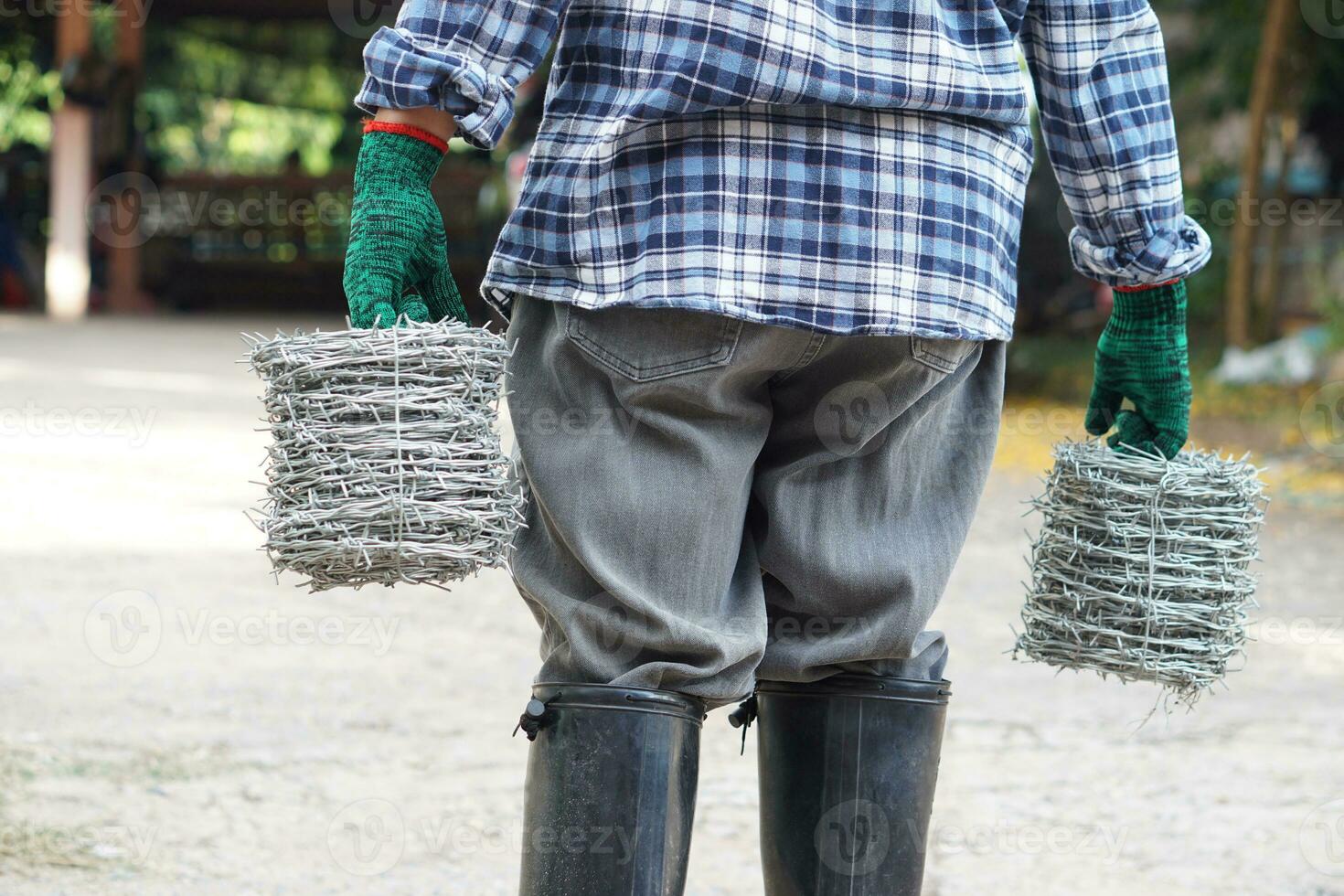 Back view of man worker is carrying rolls of metal barbed wire. Concept, construction tool. Barbed wire is used for make fences , secure property ,make border to show the territory of area. photo