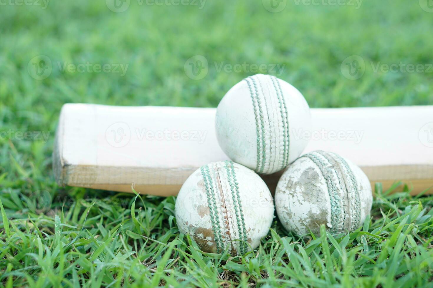 White cricket ball on wooden bat. Concept, sport equipment. Competitive sport. A cricket ball is made with a core of cork, covered by a leather case with a slightly raised sewn seam photo