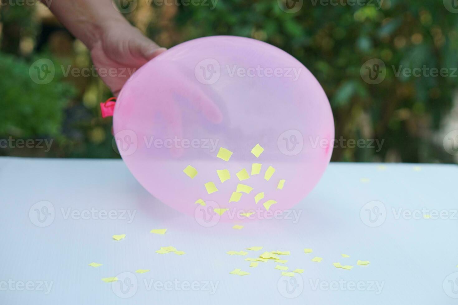 Closeup hand hold pink balloon to do science experiment about static electricity from balloon and pieces of paper. Concept, Science lesson, fun and easy experiment. Education. Teaching aids. photo