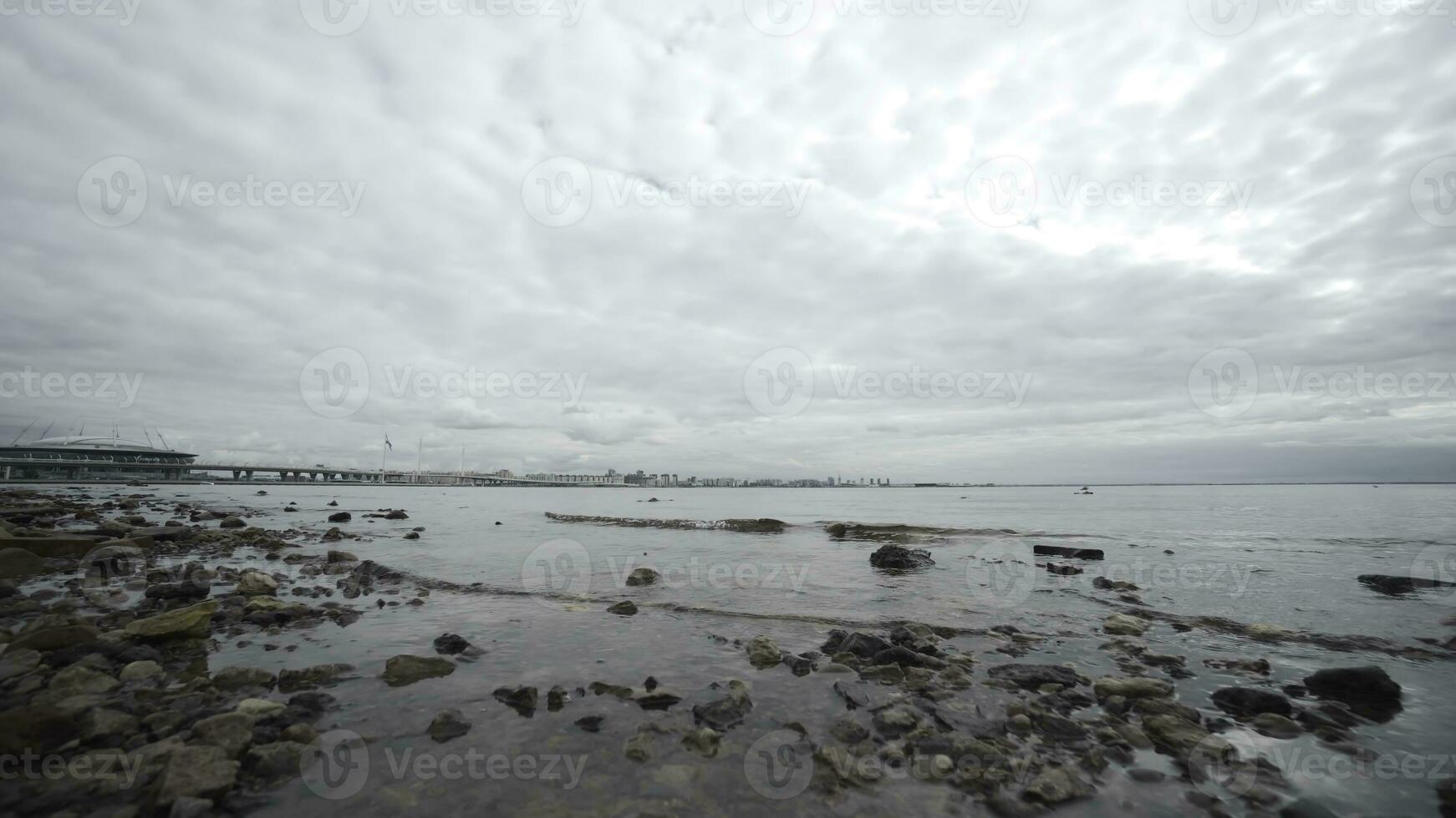 Bottom view of rocky beach and sea in cloudy weather. Action. Beautiful autumn sea with rocky beach and cloudy sky. Rocky beach on background of city on horizon and cloudy sky photo