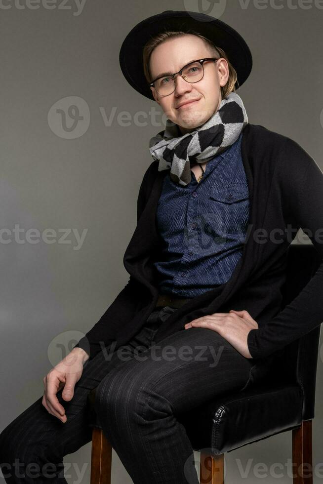 Brunet man in a casual dark clothes posing over a grey background sitting on the bar chair. photo