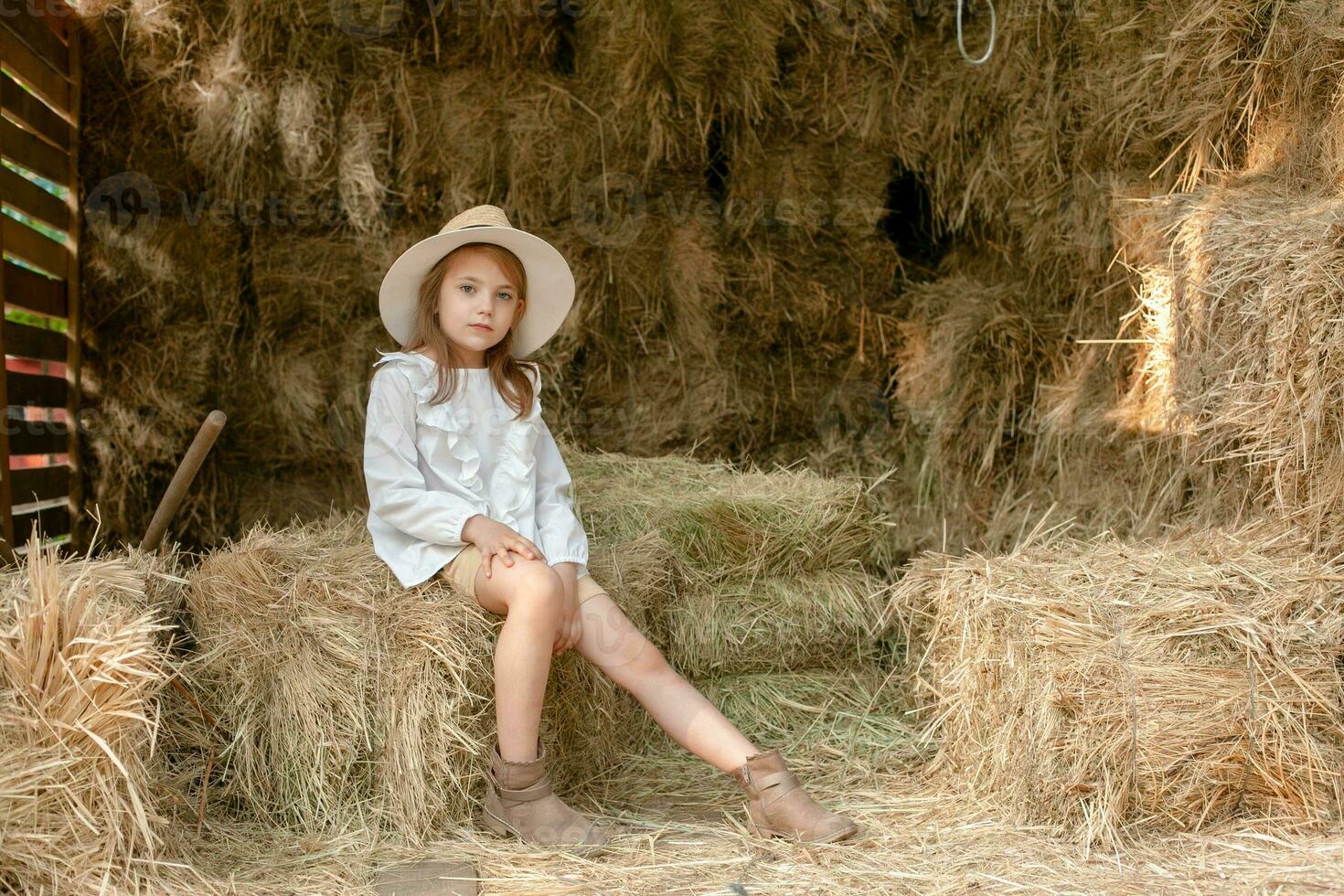 Preteen girl resting on haystack in hayloft during summer country holidays photo