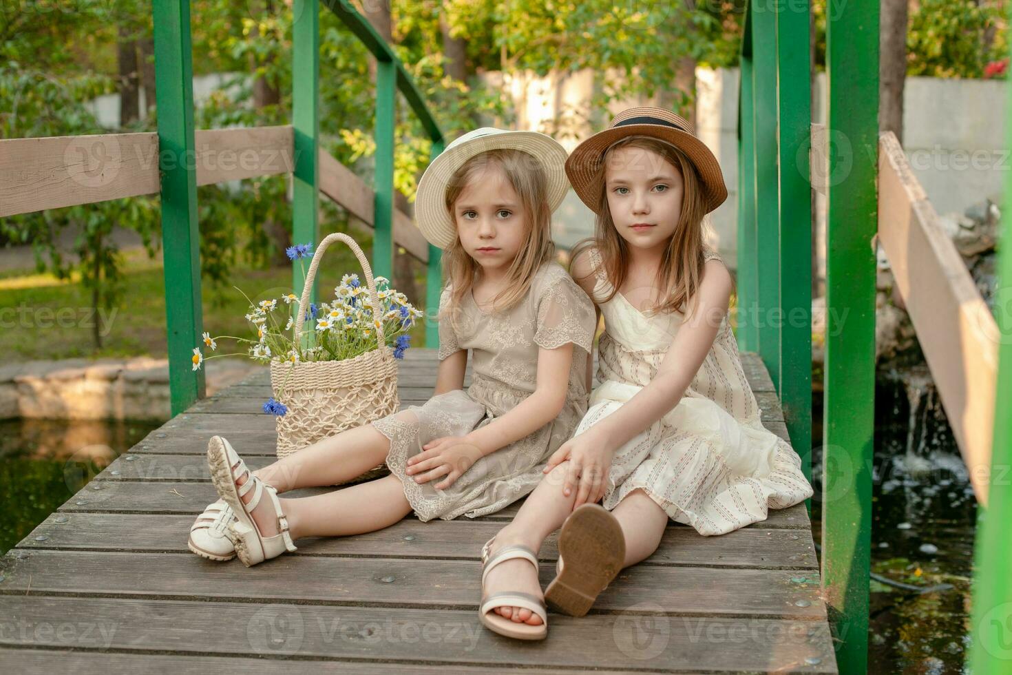 Two preteen girls sitting on bridge over pond in summer country estate photo