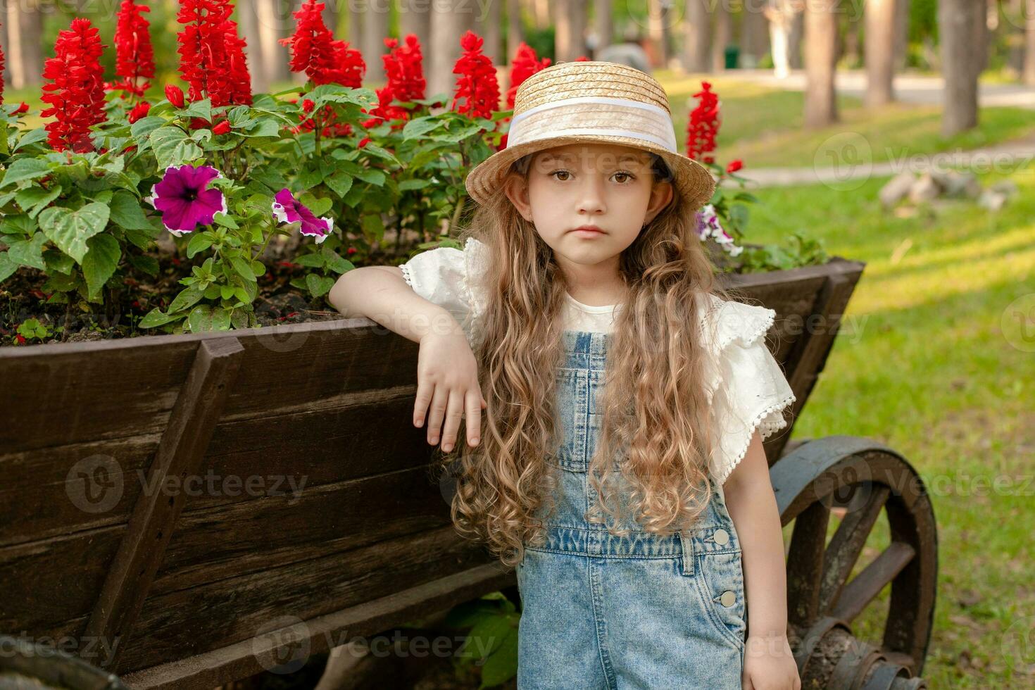Little girl leaning old wooden cart used as flowerbed in summer park photo