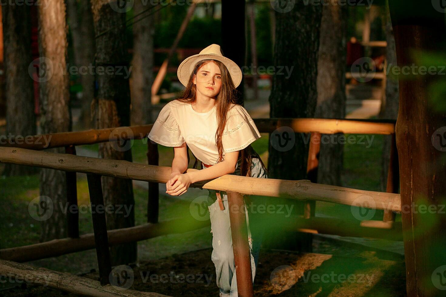 Teenage girl standing near wooden fencing in green park at dawn photo