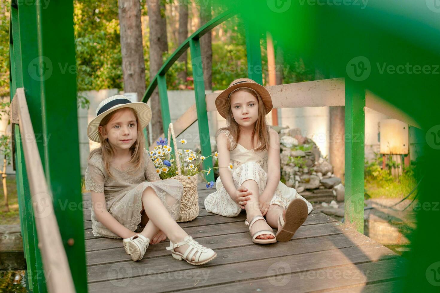Two little girls resting on wooden bridge over pond in summer country estate photo