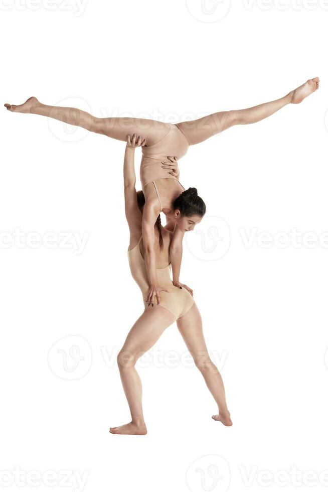 Two flexible girls gymnasts in beige leotards performing complex elements of gymnastics using support, posing isolated on white background. Close-up. photo